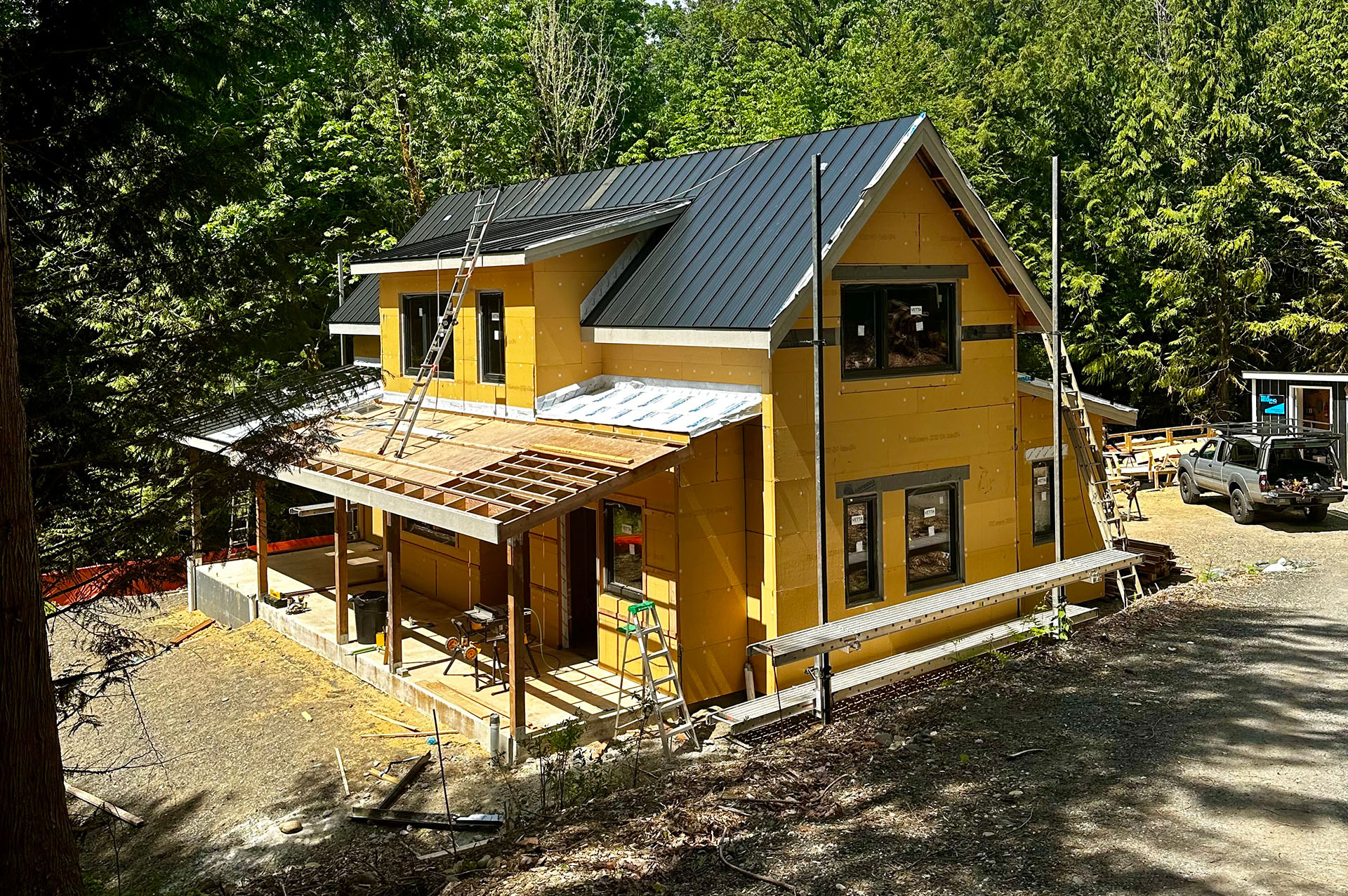 In-progress photo of a large two-story house with large windows, black metal roofing, and exterior insulation exposed.