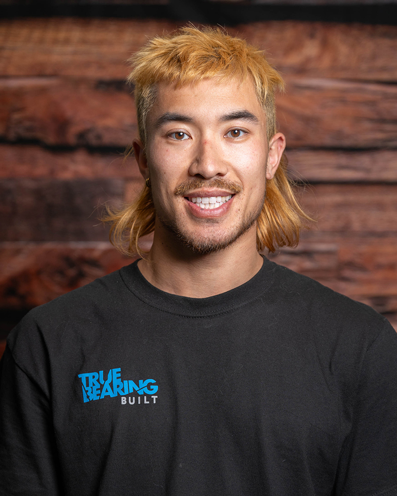 Headshot of True Bearing Built Employee, Justin Ridley, smiling in front of a wood background.