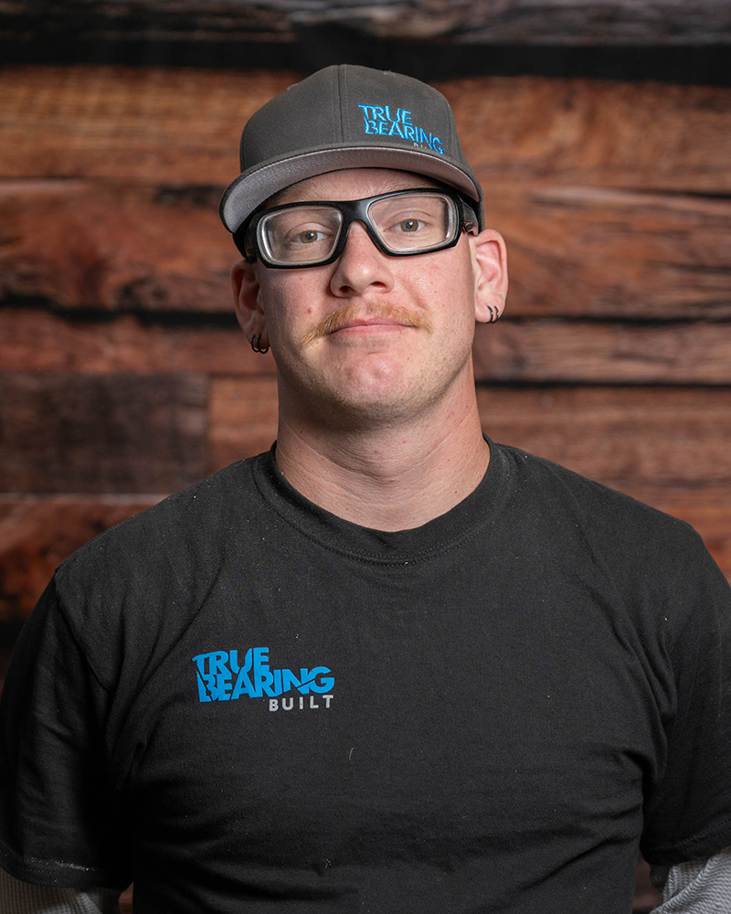 Headshot of True Bearing Built Employee, Lucas Madden, smiling in front of a wood background.