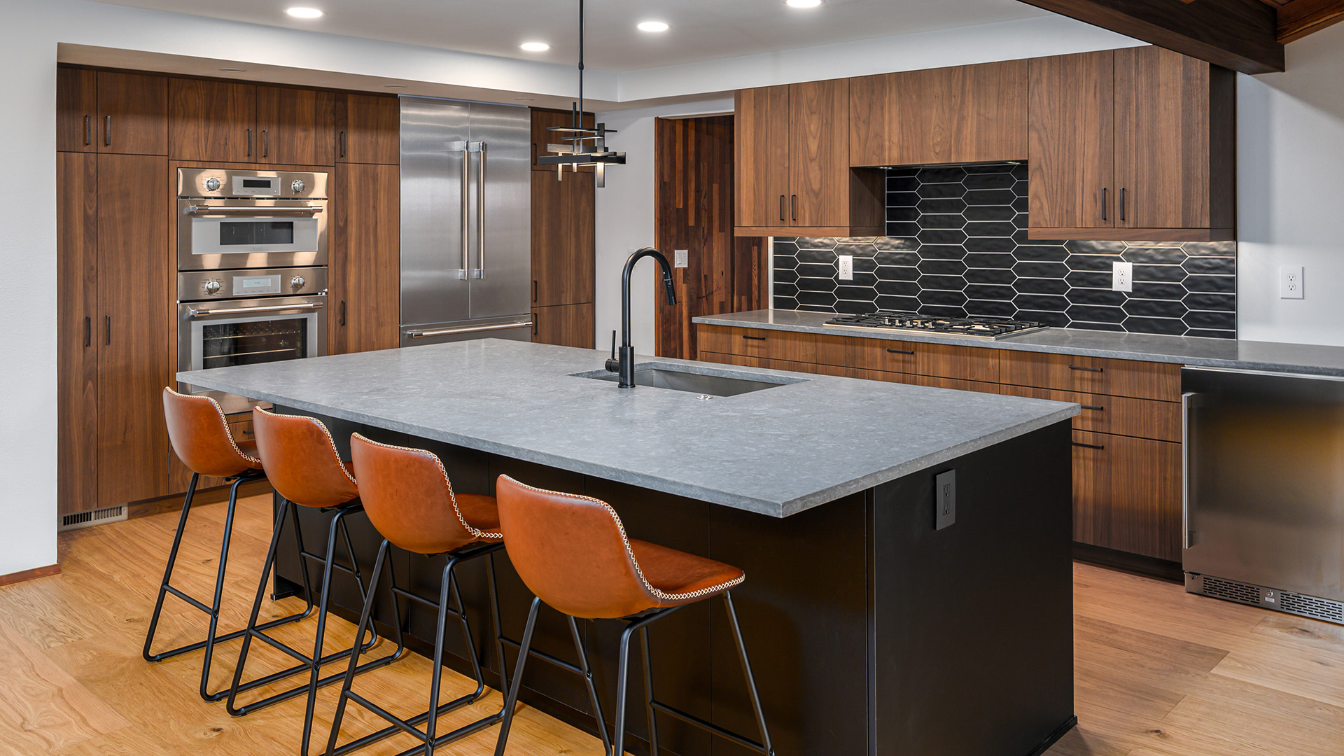 Modern kitchen layout with walnut cabinets, light gray granite countertops on the kitchen island, and 4 leather countertop stools.